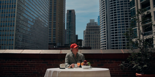 Ein Mann sitzt an einem Tisch, im Hintergrund Hochhäuser