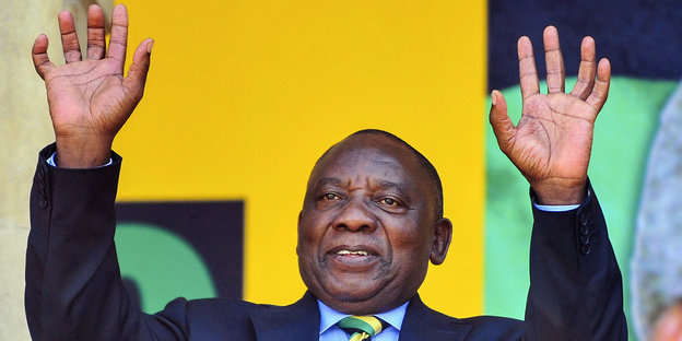 Cyril Ramaphosa gebt vor gelbem Hintergrund grüßend beide Arme