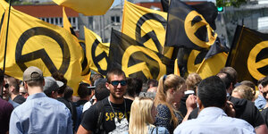 Man sieht mehrere Männer und Frauen unter gelb-schwarzen Flaggen der identitären Bewegung