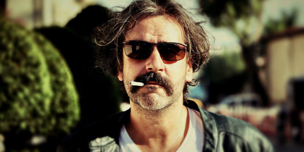 Deniz Yücel im Profil mit Sonnenbrille und einer Zigarette im Mund. Hintergrund ist unschaft.