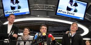 Auf zwei Bildschirmen flimmert das Foto von Deniz Yücel und seiner Frau Dilek, darunter mehrere Personen hinter Mikros