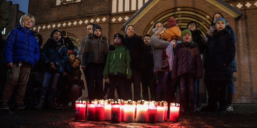 Kinder und ihre Eltern stehen mit Grablichtern vor dem Dom in St. Georg.