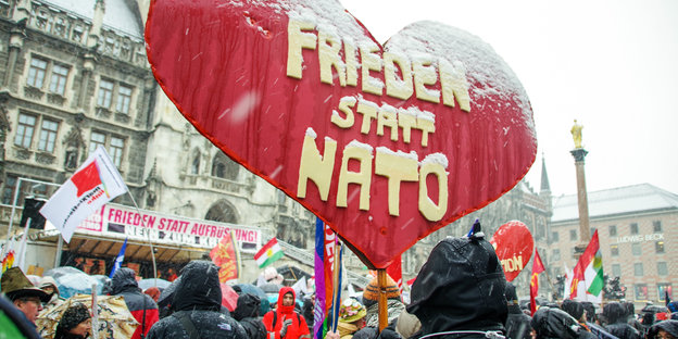 Kundgebung im Schnee, im Vordergrund ein herzförmiges Transparent mit der Aufschrift „Frieden statt Nato“
