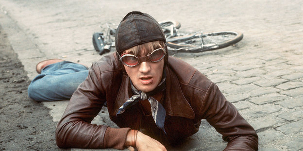 Der junge Marius Müller-Westernhagen liegt auf dem Boden. Auf dem Kopf trägt er eine Ledermütze und Fliegerbrille