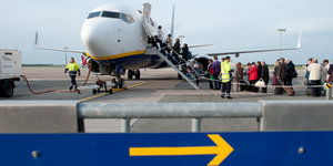Ein Flugzeug steht auf einem Rollfeld. Passagiere steigen über eine Treppe ein.