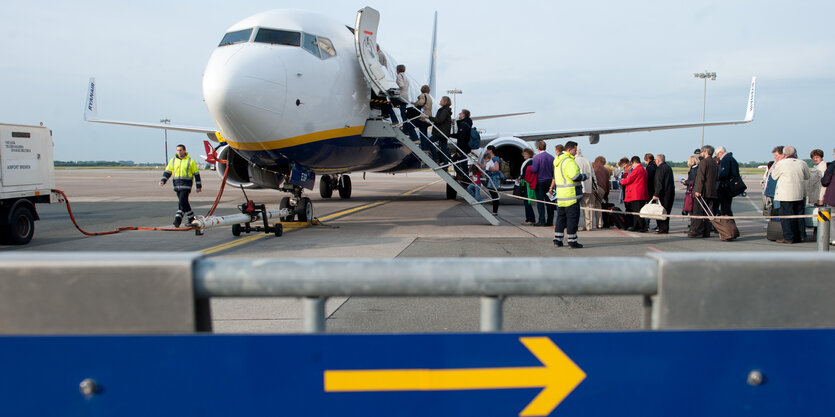 Ein Flugzeug steht auf einem Rollfeld. Passagiere steigen über eine Treppe ein.