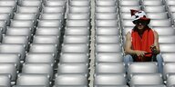 Ein Mann mit Fußallhut sitzt ganz allein in den Sitzreihen eines Stadions