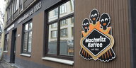 Eine braune Hausfassade mit dem Logo der Firma Machwitz. Das Logo zeigt drei Schwarze mit dicken Lippen und Glubschaugen.