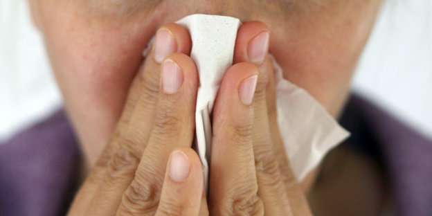 Eine Person hält sich ein Taschentuch vor die Nase.