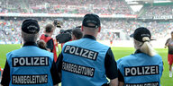 Drei Polizisten von hinten stehen vor einem Fußballfeld