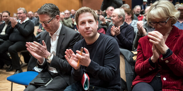 links zwei Männer, aplaudierend, rechts daneben eine Frau