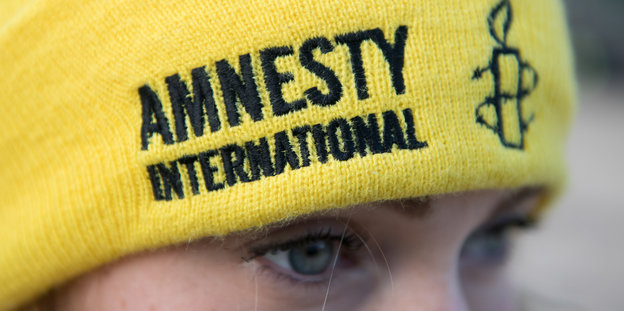 Eine Frau mit einer gelben Mütze mit dem Amnesty-Logo