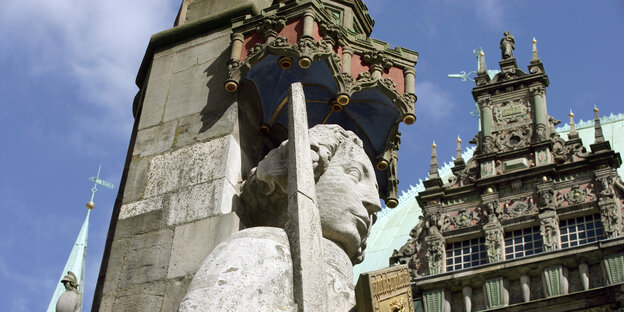 Eine Statue aus Stein zeigt einen Mann mit Schwert. Im Hintergrund steht das Bremer Rathaus.