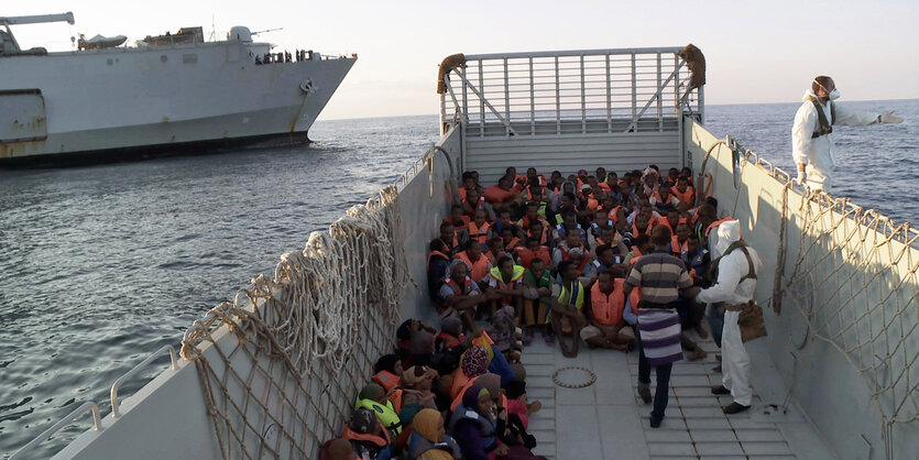 Geflüchtete sitzen in roten Rettungswesten auf einem Boot