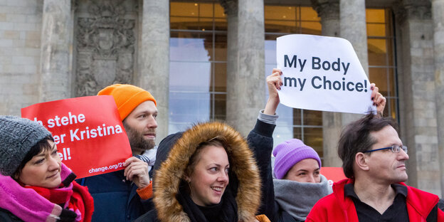 Mehrere Menschen stehen mit Plakaten vor dem Bundestag