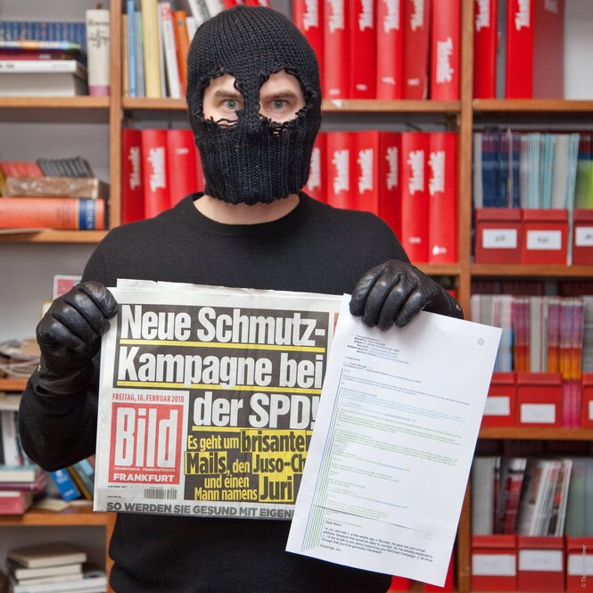 Ein maskierter Mann hält eine Ausgabe der„Bild“-Zeitung in der Hand