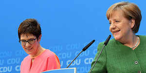 Angela Merkel und Annegret Kramp-Karrenbauer vor Pulten