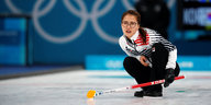 Eine Curling-Spielerin hockt nach ihrem Zug auf dem Eis