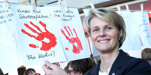 Anja Karliczek mit Plakat, das rote Hände zeigt