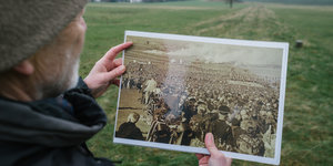 Ein Mann hält ein schwarz-weiß Foto auf dem ein Aufmarsch zu einem so genanntes Reichserntedankfest der Nazi zu sehen ist.