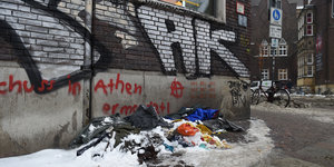Verschiedene Decken eines Obdachlosen liegen vor einer mit Graffiti besprühten Hauswand. Auf den Decken liegt teilweise Schnee.