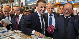 Macron steht lächelnd in einem Buchladen, um ihn herum viele ältere Männer