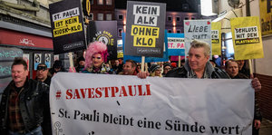 Menschen mit Plakaten und einem Transparent gehen durch eine Straße auf St. Pauli. Auf dem Transparent steht "St. Pauli ist eine Sünde wert".