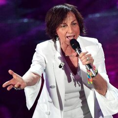 Gianna Nannini singt im weißen Anzug auf der Bühne und streckt den rechten Arm vor sich