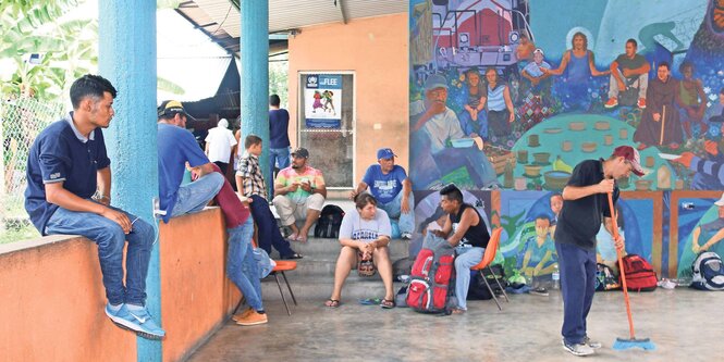 Männer, Frauen und Kinder sitzen wartend auf einer überdachten Terrasse