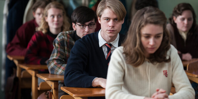 In Schulbänken sitzen Schüler_innen mit ernsten Gesichtern