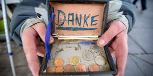 Jemand hält eine Schachtel, in der Geldmünzen liegen. Im Deckel eine Zettel mit der Aufschrift „Danke“