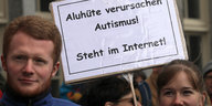 Zwei Menschen zwischen denen ein Schild in die Höhe ragt, das die Aufschrift „Aluhüte verursachen Autismus! Steht im Internet" steht