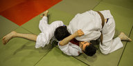 Zwei junge Männer kämpfen in Judo-Anzügen auf dem Boden einer Turnhalle.
