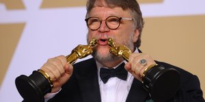 Ein Mann mit Brille küsst zwei Oscars