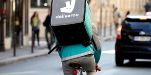 Es scheint. Ein Mensch steht mit einer Deliveroo-Tasche auf der Straße