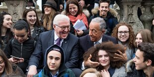 Zwei Politiker und Kinder posieren. Ein Politiker fasst einem Kind in die Haare. Die Politiker lachen