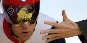 Eine Hand streckt sich in Richtung des Gesichts eines Mannes mit Brille und Helm aus