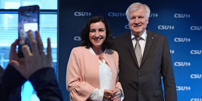 Dorothee Bär und Horst Seehofer posieren vor einer CSU Stellwand für ein Foto, das mit einem Handy aufgenommen wird