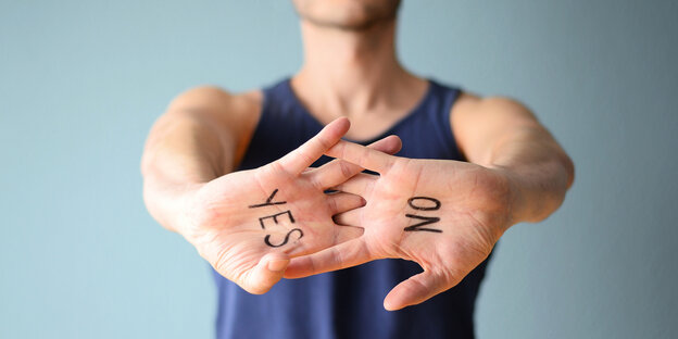 ein Mann zeigt die Innenflächen seiner verschränkten Hände. Auf einer Hand steht "No", auf der anderen "Yes"