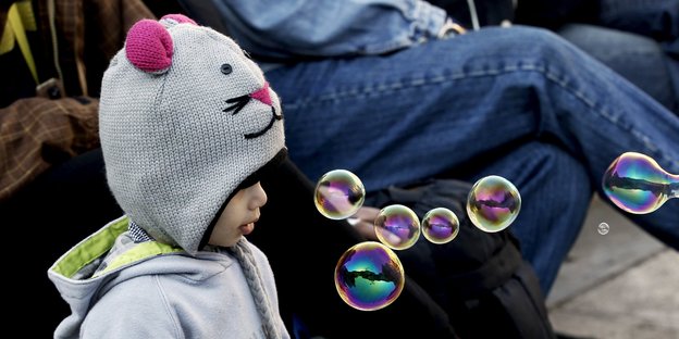 Ein Kind mit gestrickter Mausmütze schaut sich Seifenblasen an