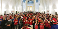 ganz viele Menschen vornehmlich in roten T-Shirts stehen in einer klassizistischen Halle