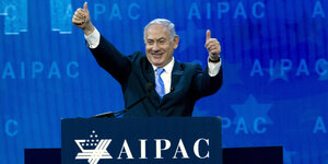 Ein Mann, Benjamin Netanjahu, steht an einem Rednerpult und streckt beide Daumen nach oben