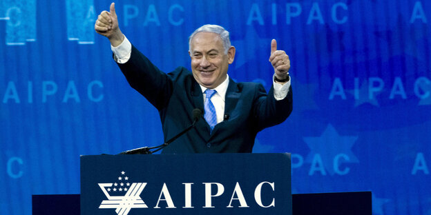 Ein Mann, Benjamin Netanjahu, steht an einem Rednerpult und streckt beide Daumen nach oben