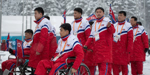 Mehrere Sportler in einheitlichen Trainingsbekleidung im Schnee, darunter auch Rollstuhlfahrer
