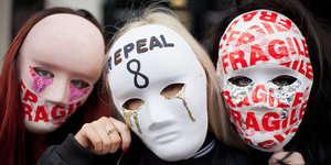 Drei Menschen tragen Masken im Gesicht, auf denen „Fragile“ und „Repeal“ steht