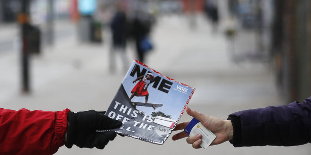 Eine NME-Ausgabe wird von zwei ausgestreckten Händen gehalten - im Hintergrund eine Straßenszenerie
