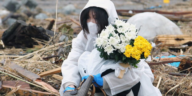 Eine Frau betet und legt Blumen nieder an der Stelle an der ihr Haus stand, das durch den Tsunami, der auch das nahegelegene Kernkraftwerk Fukushima beschädigt hat, zerstört wurde
