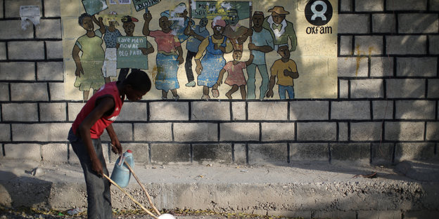Ein Junge spielt in einem Flüchtlngscamp auf Haiti vor einer Wand, auf der das Oxfam-Logo aufgemalt ist