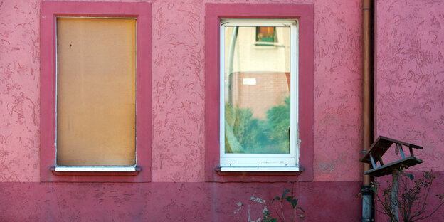 Eine pinke Hauswand, zwei Fenster sind mit Holz versperrt