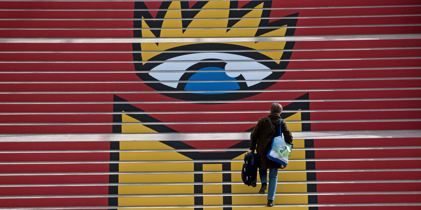 Eine Frau steigt in der Glashalle der Neuen Messe in Leipzig eine Treppe mit dem Logo der Leipziger Buchmesse hinauf.